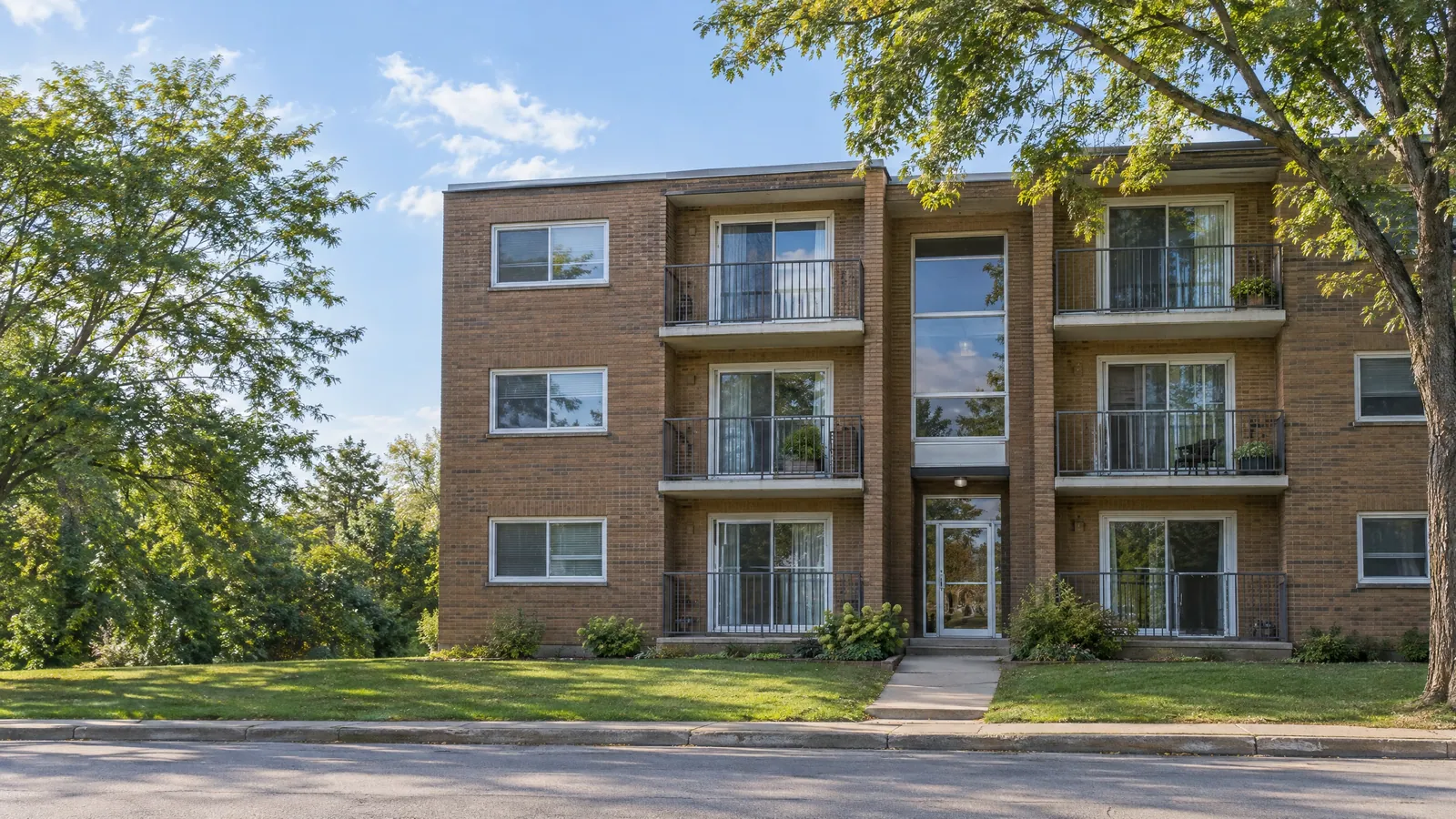 Three-storey brick walk-up apartment building with slider windows and a small balcony at each suite
