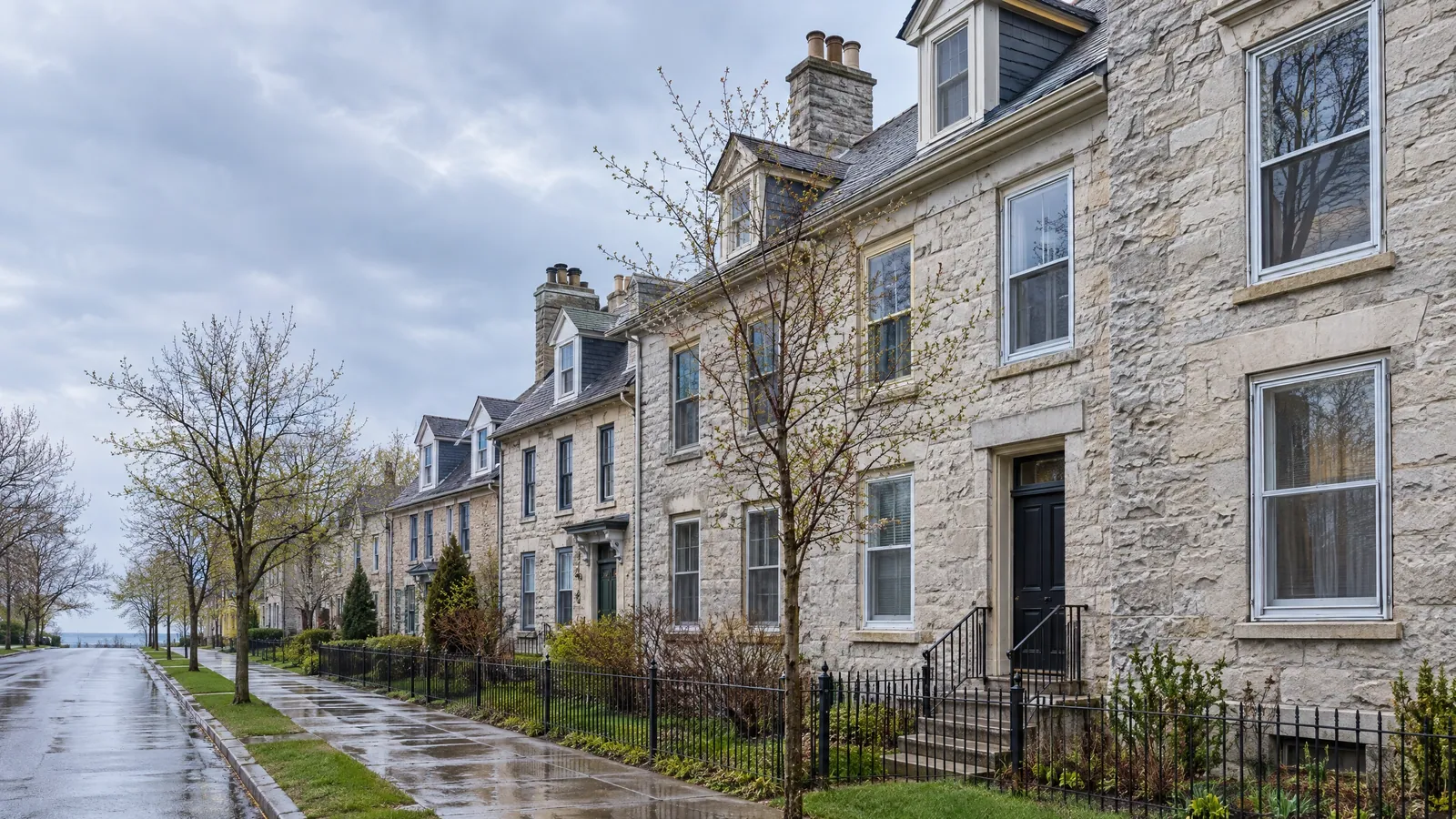 Quiet street of attached limestone houses with tall wood sash windows and stone sills, the pavement still wet after spring rain