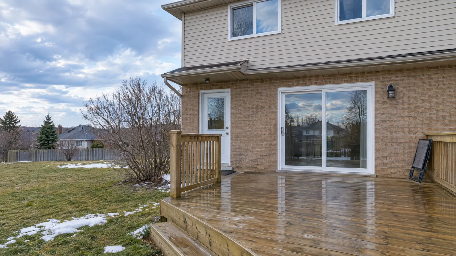 Back of a brick and vinyl-sided house with a white sliding patio door and a half-glass hinged garden door, both opening onto a wooden deck